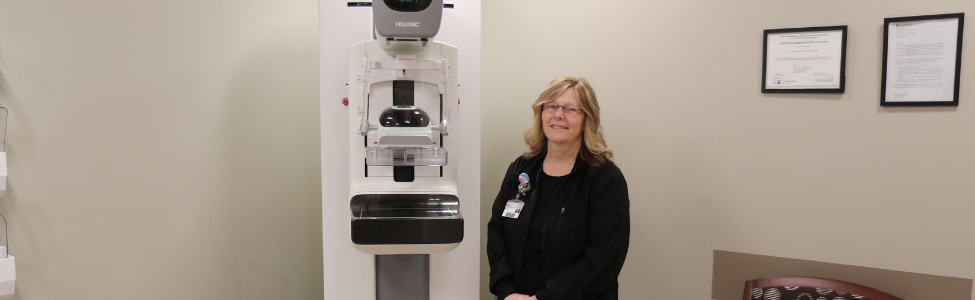 A mammography tech standing next to a 3D mammography machine. 