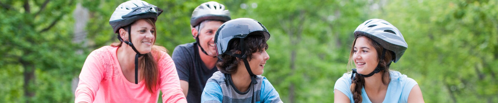 Family riding bikes in a park and wearing helmets 